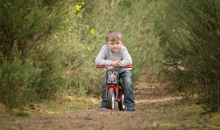 Eion posing with his little balance bike in Elstead, Surrey. Sarah Angel Photography Farnham Bike Race Charity photography project.